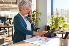 Operations manager pressing a phone keypad with a call flowchart on her desk